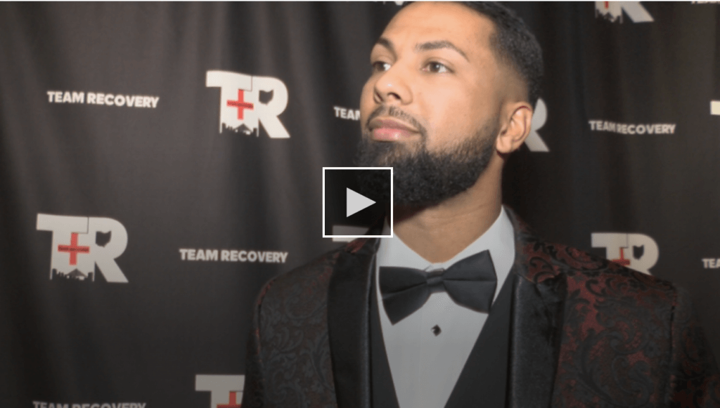 screenshot of man standing in front of team recovery logo