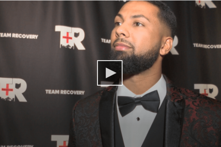 screenshot of man standing in front of team recovery logo