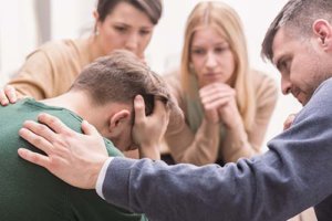 man with head down getting support during family therapy program