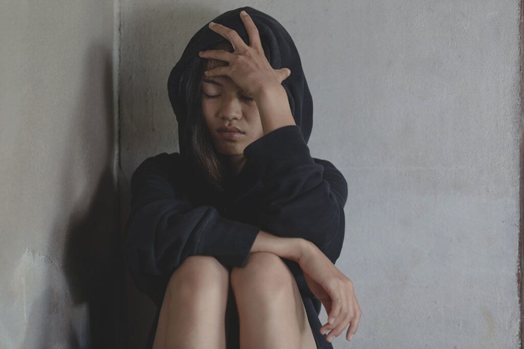 young woman sitting holding her head starting to experience Heroin Overdose Symptoms