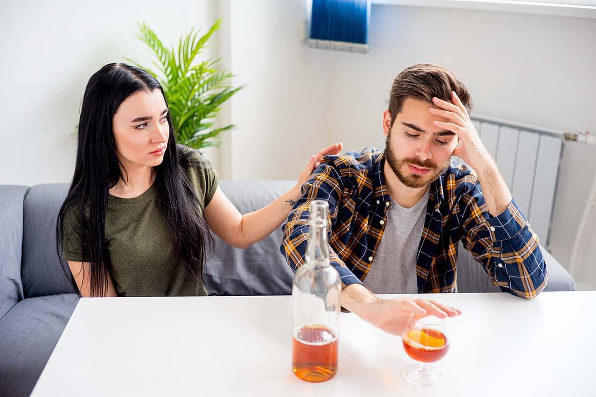 woman putting a hand on her drinking husband wondering How to Help an Alcoholic