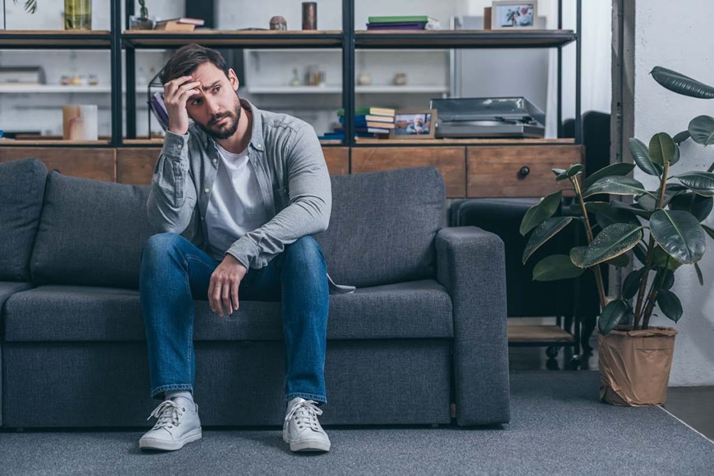 a man sitting on a couch thinking about heroin withdrawal symptoms