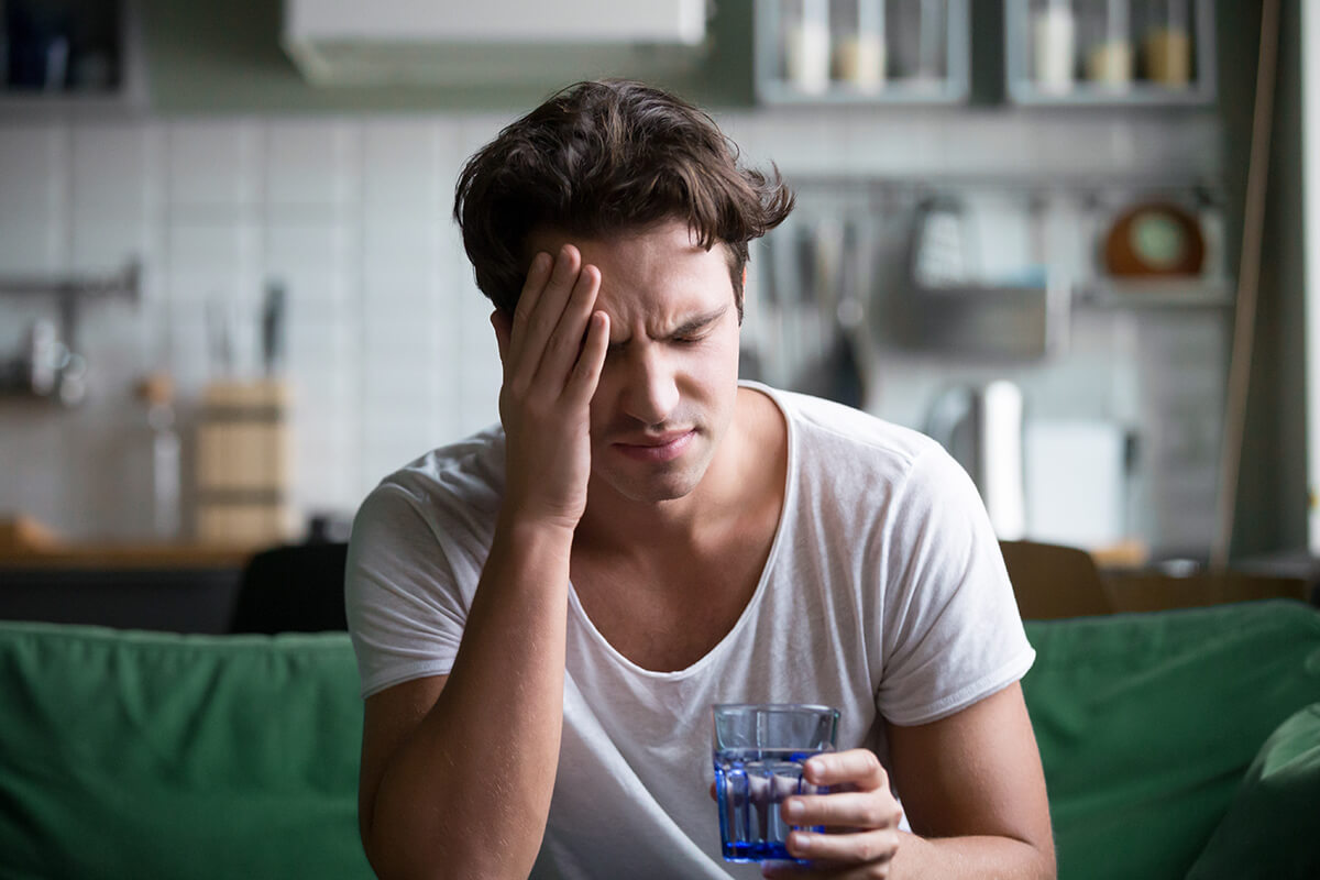 man drinking water holding his head recovering from the Signs of Alcohol Overdose