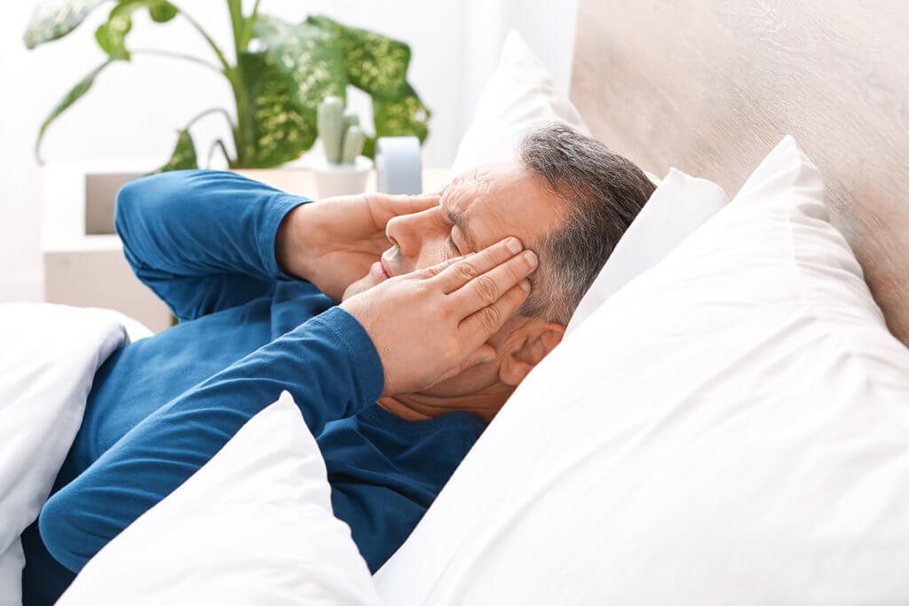 man rubbing his temples in bed going through the Xanax Withdrawal Timeline