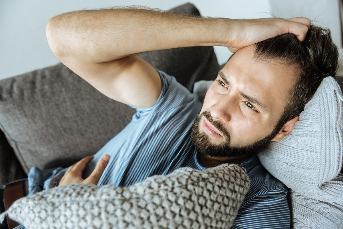 man grabbing his hair laying on couch going through Symptoms of Addiction