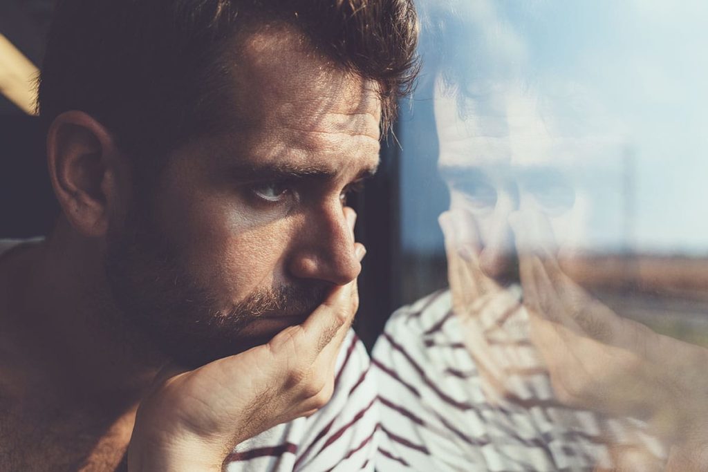 a man looking out a window thinking about the signs of a xanax addiction