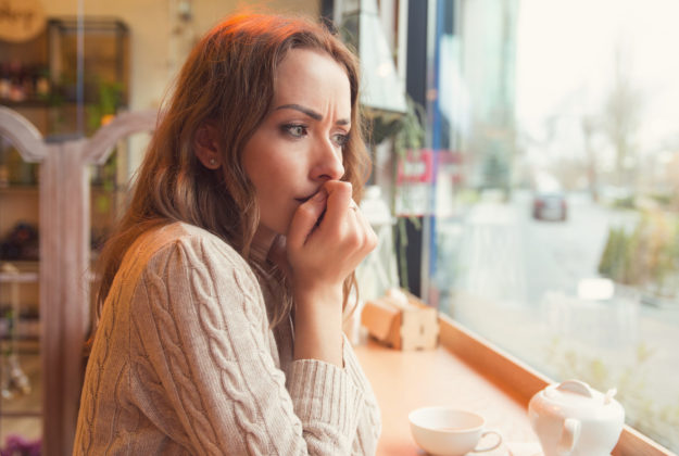 Nervous woman biting nails and looking away sitting alone in a coffee shop woman struggles with getting past her alcohol cravings