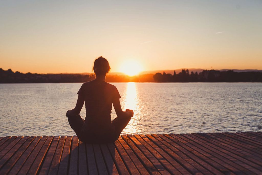 a person meditating by water thinking about the benefits of holistic therapy
