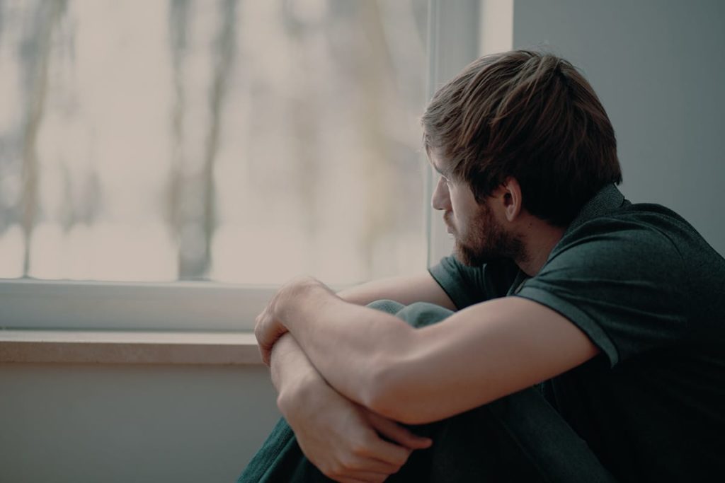 a man looking out a window wondering is marijuana addictive