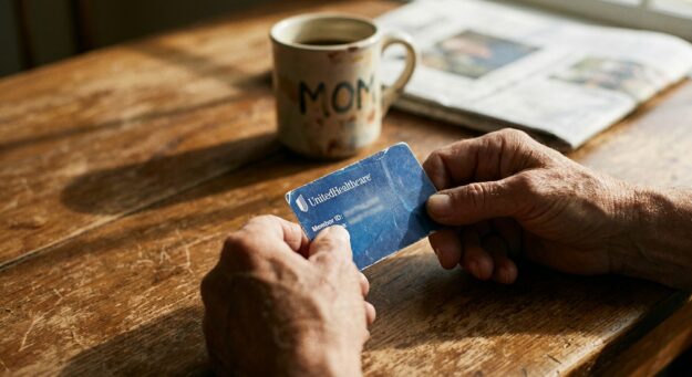 Parent's hands holding UnitedHealthcare insurance card at kitchen table, representing the moment before calling about detox coverage